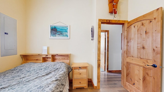 bedroom with electric panel, wood finished floors, and baseboards