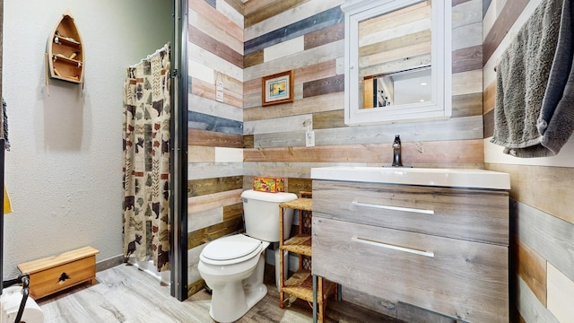 bathroom with wooden walls, a shower stall, toilet, and vanity