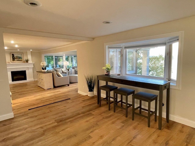 dining area with a large fireplace, baseboards, crown molding, and light wood finished floors