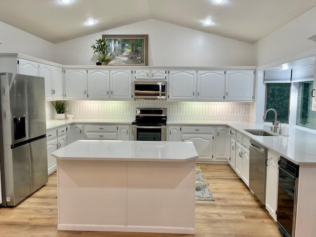 kitchen with stainless steel appliances, light wood-type flooring, a sink, and lofted ceiling