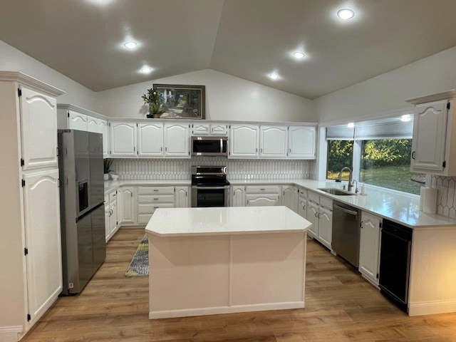 kitchen featuring light wood-style flooring, a kitchen island, appliances with stainless steel finishes, a sink, and backsplash