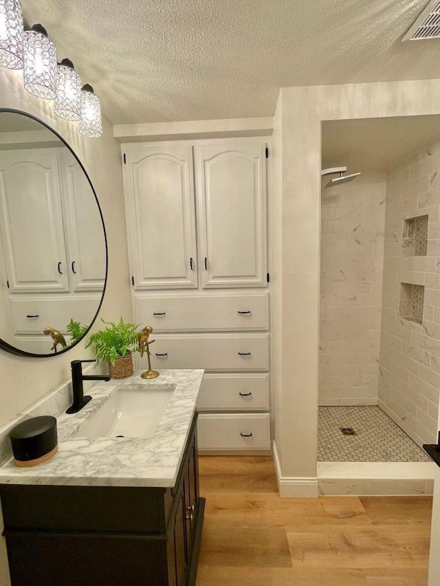 full bath featuring visible vents, a tile shower, wood finished floors, and vanity