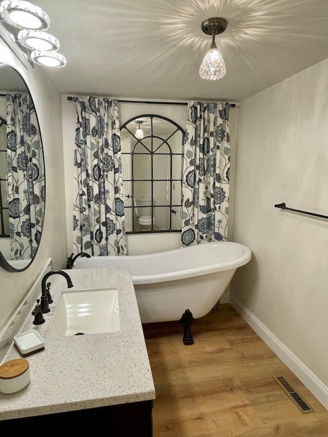 bathroom with visible vents, vanity, wood finished floors, a freestanding tub, and baseboards