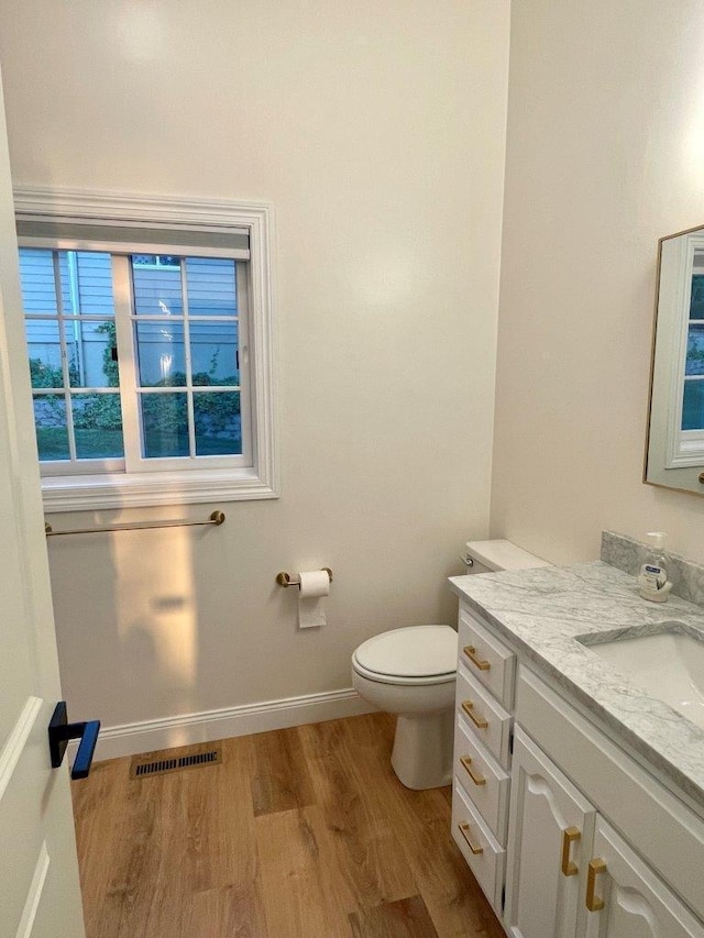 half bath with baseboards, visible vents, toilet, wood finished floors, and vanity