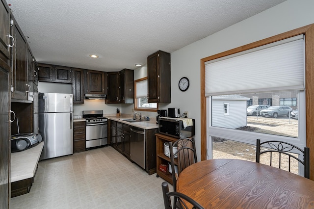 kitchen with a sink, light countertops, under cabinet range hood, a textured ceiling, and appliances with stainless steel finishes