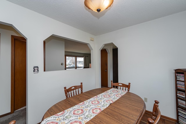 dining room featuring baseboards, arched walkways, a textured ceiling, and carpet