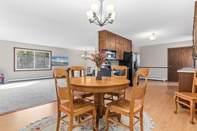 dining room with a chandelier, baseboard heating, and light wood finished floors