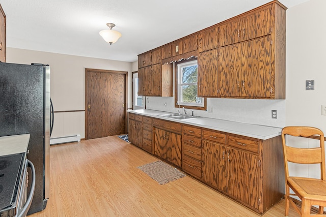 kitchen featuring a sink, baseboard heating, light wood-style flooring, and light countertops