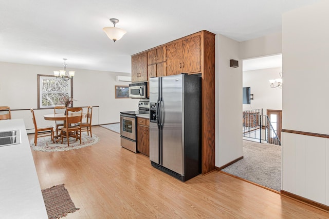 kitchen featuring brown cabinets, a wall unit AC, stainless steel appliances, an inviting chandelier, and light wood finished floors