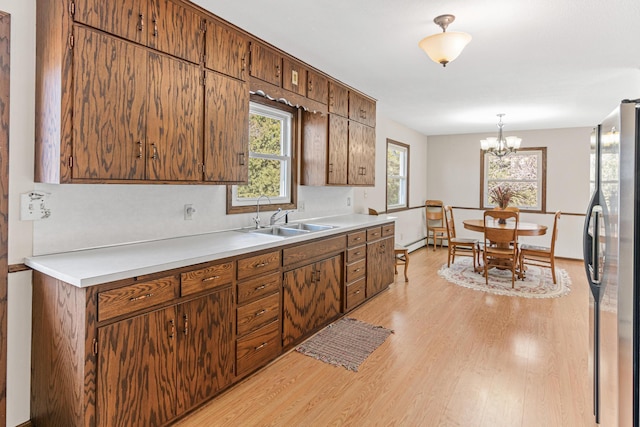 kitchen featuring light wood-style flooring, freestanding refrigerator, a sink, light countertops, and decorative light fixtures