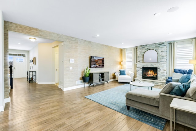 living room featuring light wood finished floors, recessed lighting, baseboards, and a stone fireplace