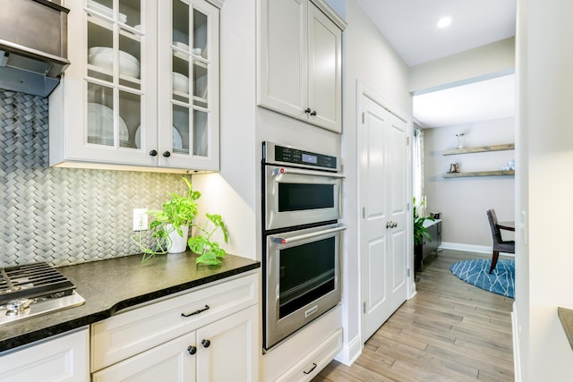 kitchen featuring tasteful backsplash, dark countertops, light wood-style flooring, glass insert cabinets, and double oven