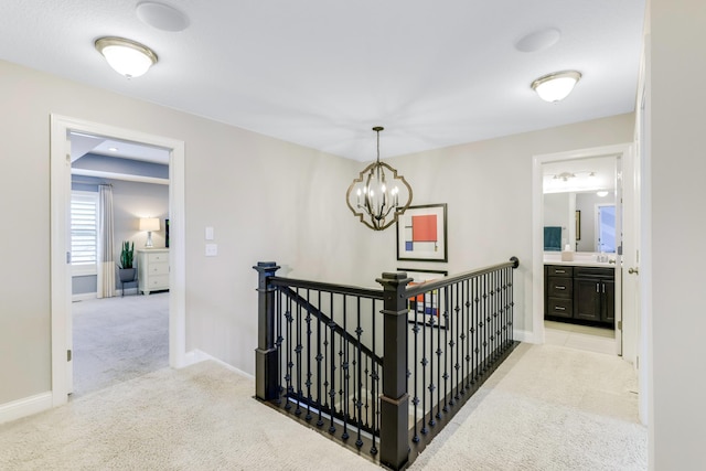 hall featuring baseboards, light carpet, an upstairs landing, and an inviting chandelier