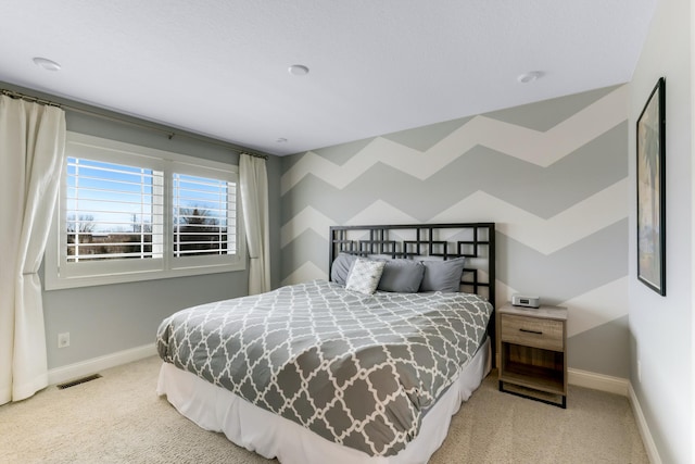 carpeted bedroom with an accent wall, visible vents, and baseboards