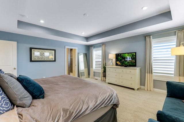 bedroom featuring a raised ceiling, light carpet, and baseboards