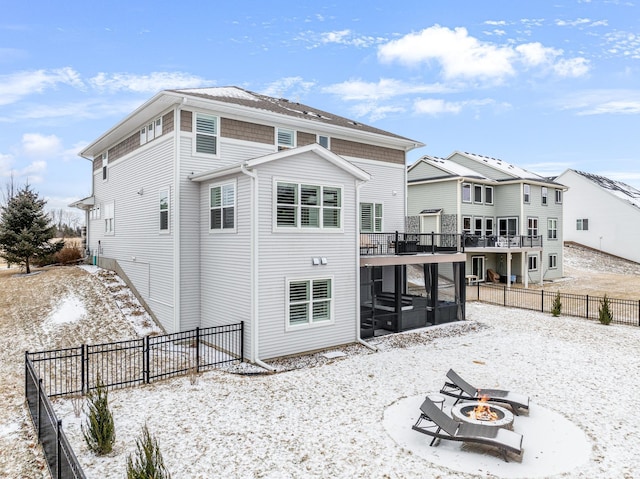 snow covered property featuring a fire pit, a fenced backyard, and a sunroom