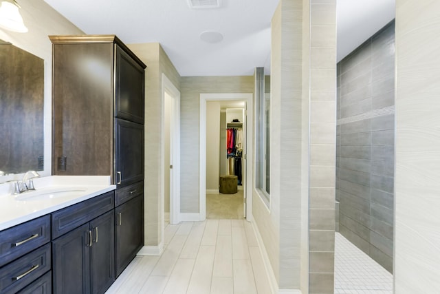 bathroom with a spacious closet, baseboards, a walk in shower, and vanity