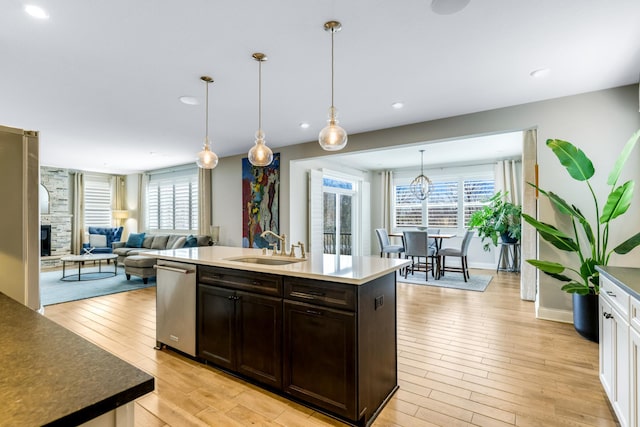 kitchen featuring dark brown cabinetry, a sink, a stone fireplace, light wood-style floors, and stainless steel dishwasher