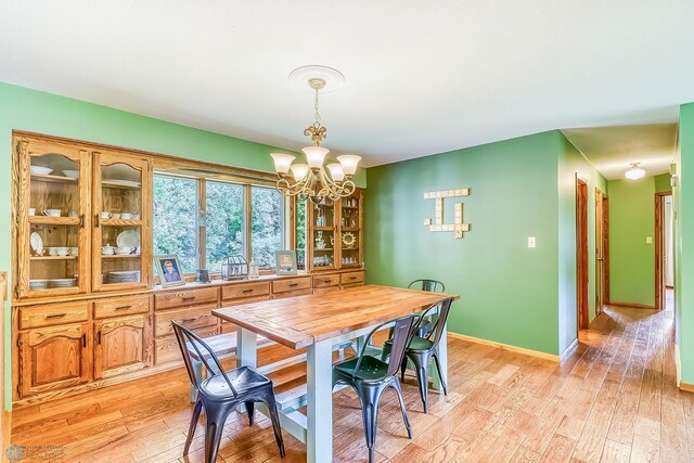 dining room with light wood-type flooring, baseboards, and an inviting chandelier