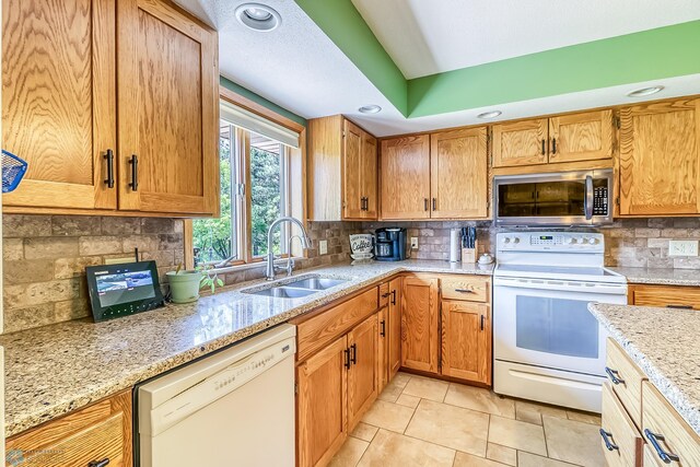 kitchen featuring light stone counters, recessed lighting, backsplash, a sink, and white appliances