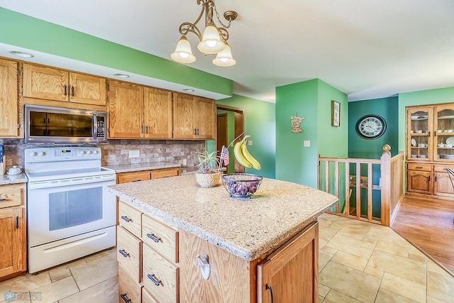 kitchen with white electric stove, a center island, light stone countertops, tasteful backsplash, and stainless steel microwave