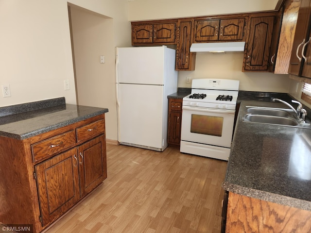 kitchen with white appliances, light wood finished floors, a sink, under cabinet range hood, and dark countertops