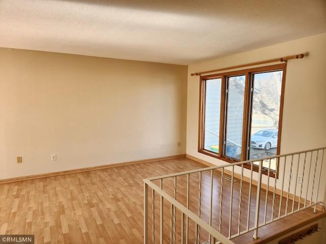 spare room with a textured ceiling, baseboards, stairs, and light wood-style floors