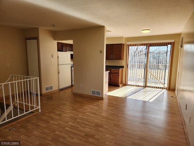 empty room with a textured ceiling, wood finished floors, visible vents, and baseboards