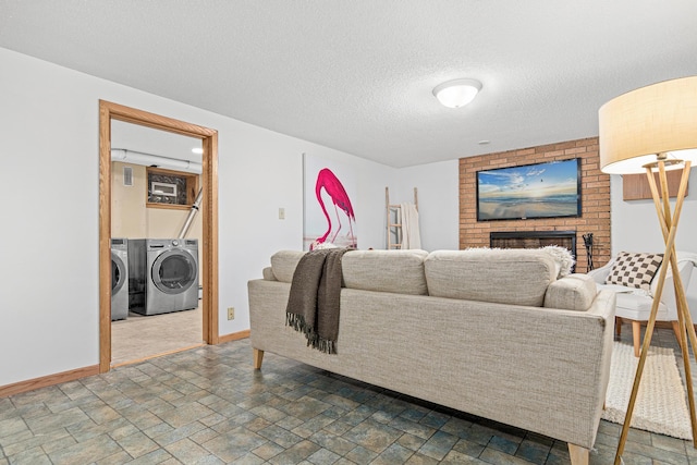 living area with independent washer and dryer, stone finish flooring, a textured ceiling, baseboards, and a brick fireplace