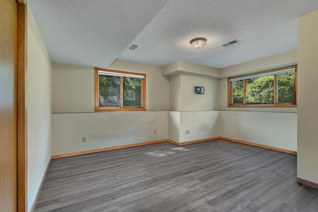 spare room featuring visible vents, a textured ceiling, baseboards, and wood finished floors