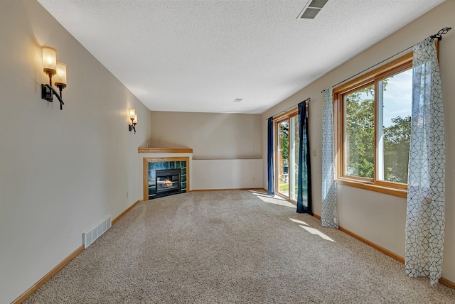 unfurnished living room featuring carpet flooring, visible vents, a textured ceiling, and a tiled fireplace