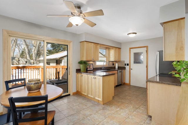 kitchen with dishwasher, light brown cabinetry, dark countertops, and a sink