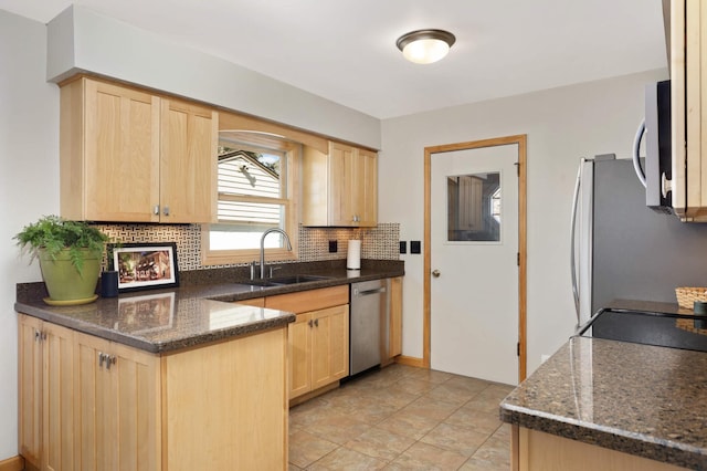 kitchen featuring decorative backsplash, dark stone countertops, stainless steel appliances, light brown cabinetry, and a sink