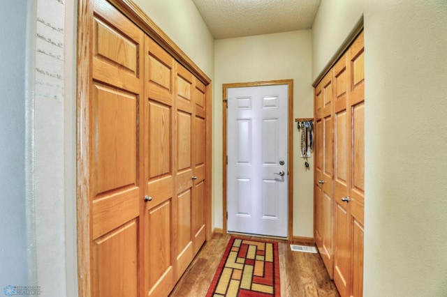 doorway featuring visible vents, baseboards, a textured ceiling, and wood finished floors