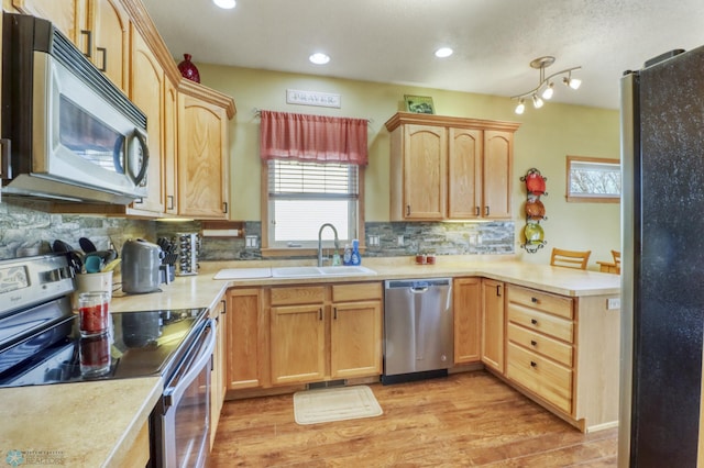 kitchen with a sink, tasteful backsplash, appliances with stainless steel finishes, a peninsula, and light countertops