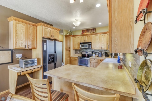 kitchen featuring light brown cabinetry, tasteful backsplash, appliances with stainless steel finishes, a peninsula, and a toaster