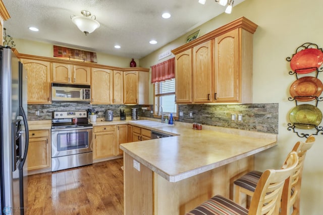 kitchen with a peninsula, light countertops, light wood-style floors, appliances with stainless steel finishes, and backsplash