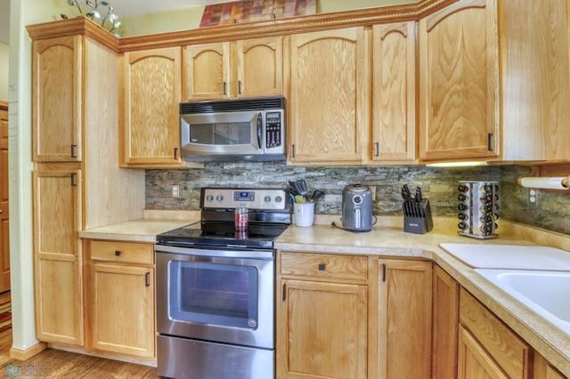 kitchen with light brown cabinets, stainless steel appliances, decorative backsplash, and light countertops