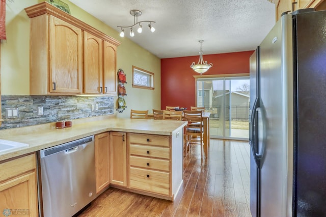 kitchen featuring light brown cabinets, a peninsula, stainless steel appliances, and light countertops