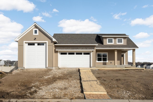 view of front of home with an attached garage, covered porch, dirt driveway, and a shingled roof