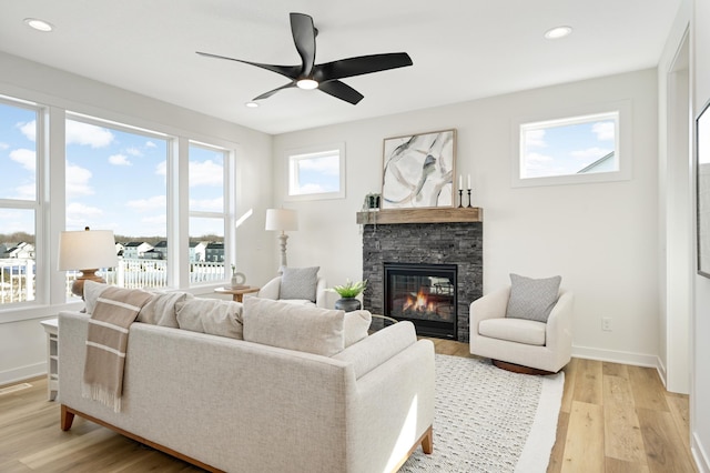 living room featuring baseboards, ceiling fan, light wood-type flooring, recessed lighting, and a fireplace