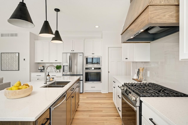 kitchen featuring visible vents, light wood-style flooring, custom exhaust hood, stainless steel appliances, and a sink