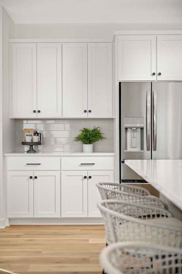 kitchen featuring light wood-style flooring, stainless steel refrigerator with ice dispenser, white cabinetry, light countertops, and decorative backsplash