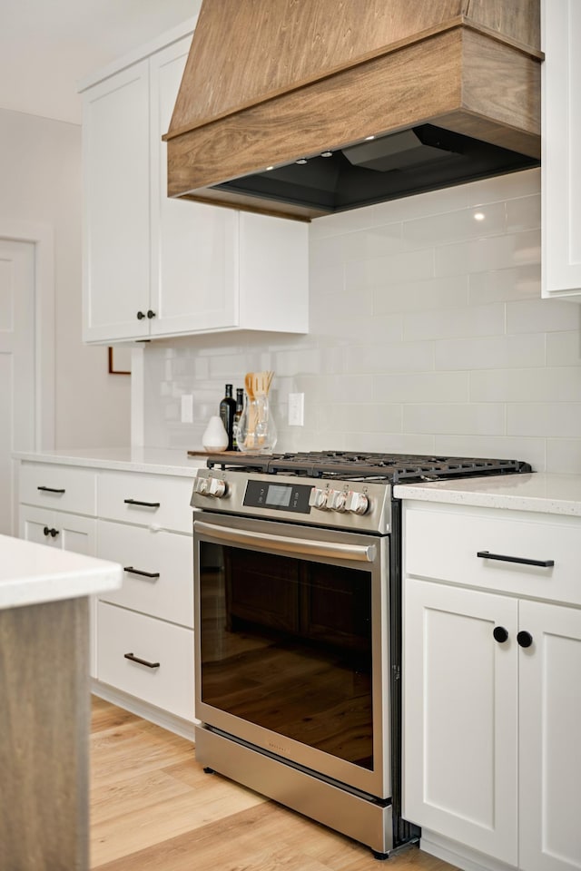 kitchen with light wood-type flooring, custom range hood, backsplash, light countertops, and stainless steel range with gas stovetop