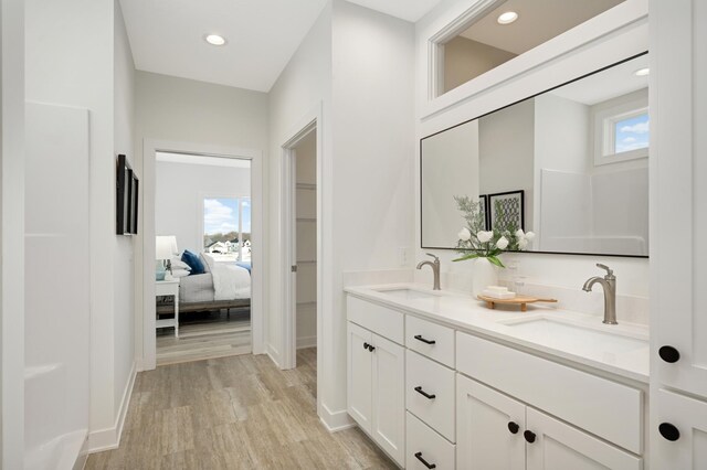 bathroom with a sink, recessed lighting, wood finished floors, and double vanity