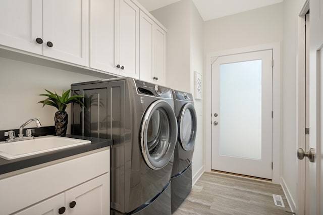 laundry area with visible vents, washer and dryer, light wood-style floors, cabinet space, and a sink