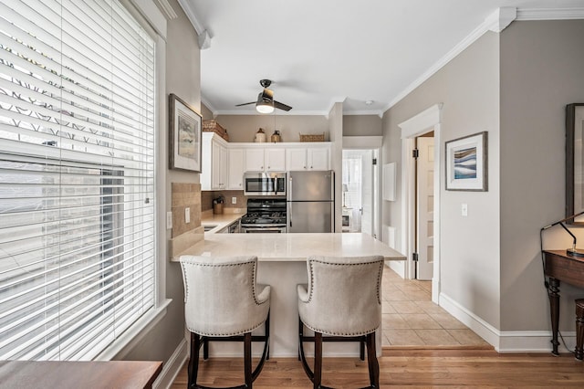 kitchen with tasteful backsplash, crown molding, stainless steel appliances, white cabinetry, and a ceiling fan