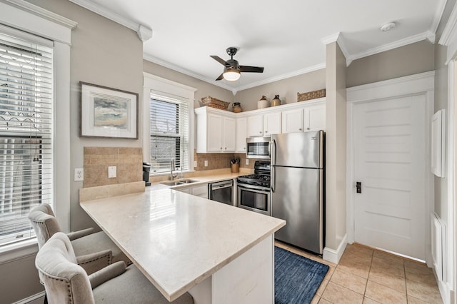 kitchen featuring light countertops, appliances with stainless steel finishes, a peninsula, white cabinetry, and a sink