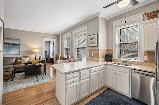 kitchen with light countertops, ornamental molding, a peninsula, stainless steel dishwasher, and a sink