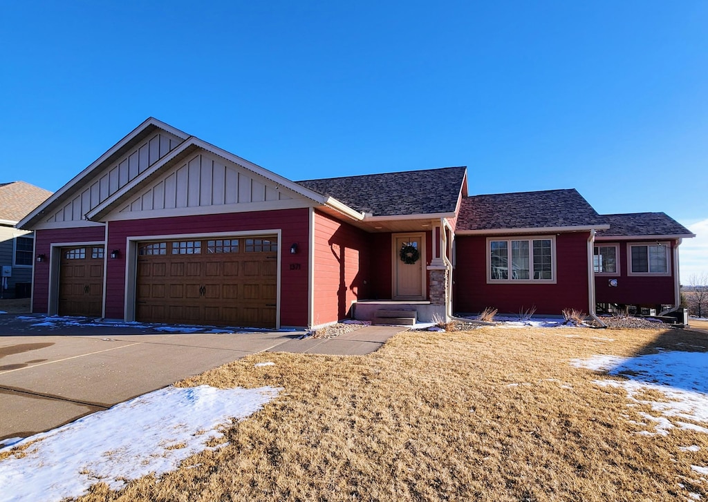 ranch-style home featuring an attached garage, a shingled roof, and board and batten siding